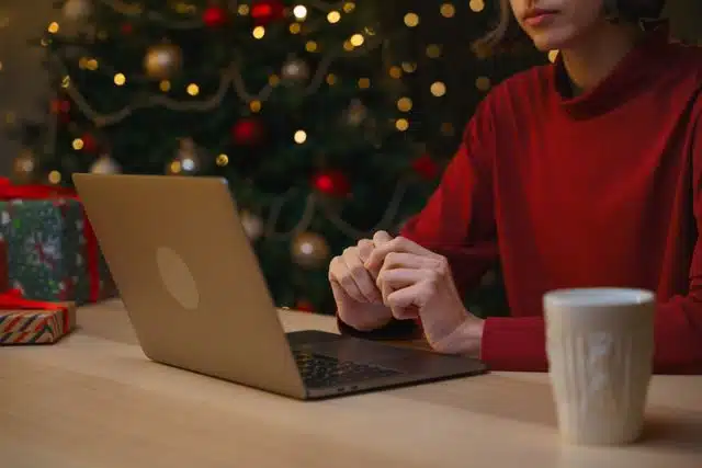 Woman in red sweater using laptop at a holiday-decorated table with gifts.