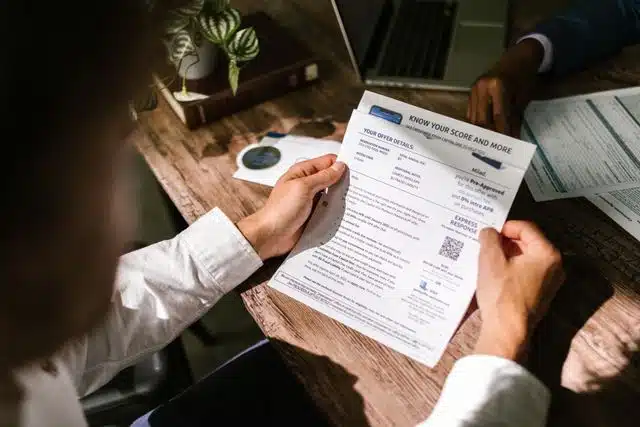 An adult man examining a financial document under natural light at a wooden desk, emphasizing finance and reading