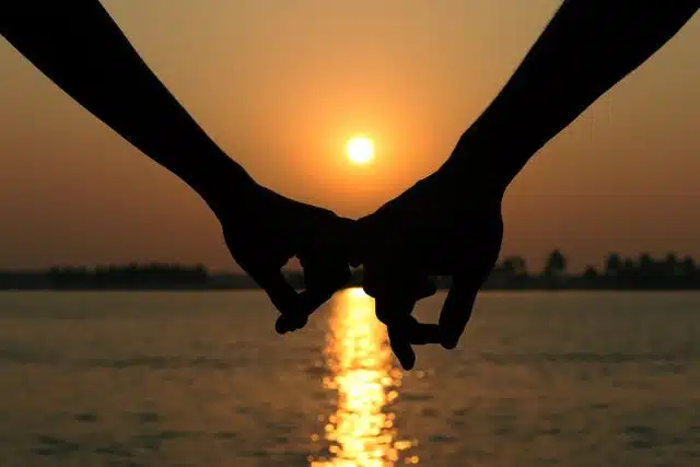 Silhouette of a couple holding hands at sunset over a serene waterscape