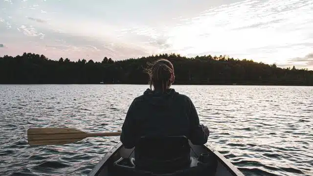 A woman paddles a canoe on a tranquil Minnesota lake at sunset, surrounded by nature.