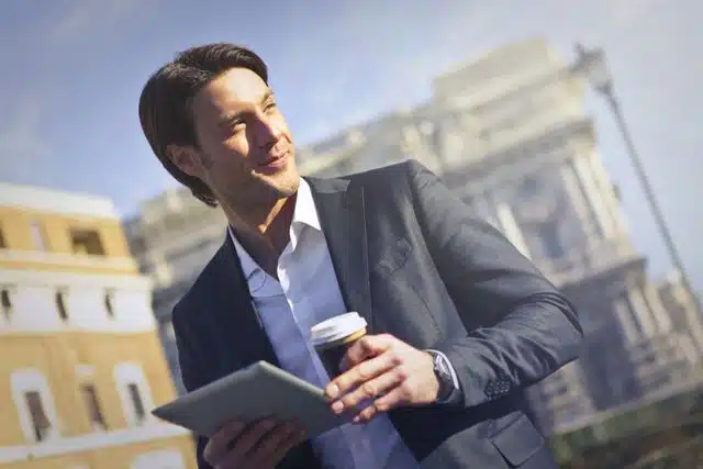 Confident businessman with tablet and coffee outdoors.